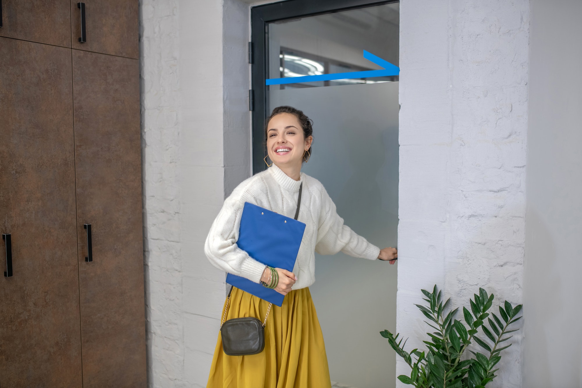 Young woman standing at the door, holding door hangle, smiling